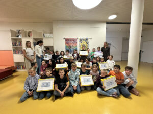 Eine Gruppe von Kindern und zwei Lehrer, die in einer Schulbibliothek mit gelben Urkunden posieren.